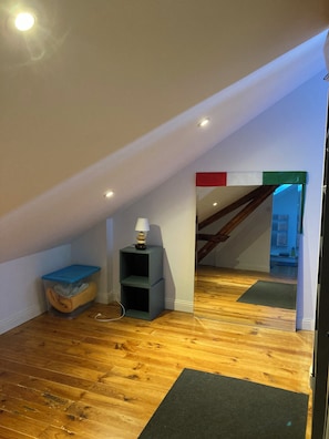 Une pièce avec un plancher en bois, une boîte de rangement bleue, une étagère grise et une lampe.