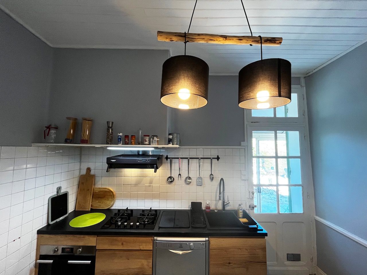 Une cuisine moderne dotée d’une cuisinière à gaz, d’un plan de travail noir, d’ustensiles suspendus et de luminaires suspendus.