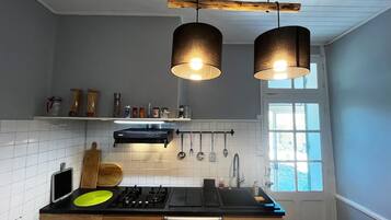Une cuisine moderne dotée d’une cuisinière à gaz, d’un plan de travail noir, d’ustensiles suspendus et de luminaires suspendus.