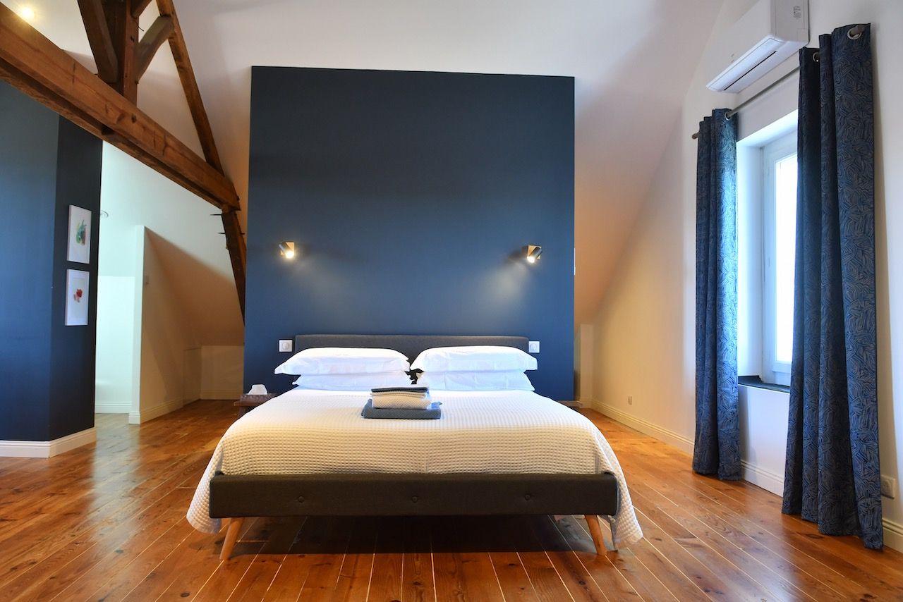 Un dormitorio con una cama grande, vigas de madera, una pared oscura y una ventana con cortinas.