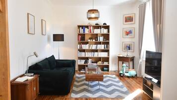 Een woonkamer met een bank, een boekenkast, een televisie en een scooter.