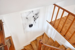 Una escalera de madera con una pared blanca y un retrato blanco y negro de un caballo enmarcado.