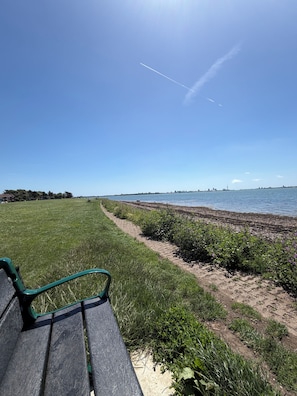 Eine Parkbank mit Blick auf einen Strand, einem klaren Himmel und einer entfernten Stadtlandschaft.