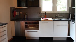 Een moderne keuken met roestvrijstalen apparatuur, witte keukenkastjes en een raam dat voor daglicht zorgt.