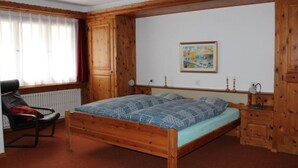 Een slaapkamer met een houten bed, een stoel, een radiator en een schilderij aan de muur.