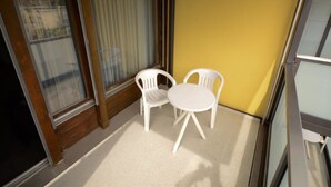 A balcony with two white plastic chairs and a small table, wooden floor, and large windows with blinds. - Touring 307 Appartement/Fewo, Dusche oder Bad, WC 1-Zimmerwohnung by Interhome (Davos)