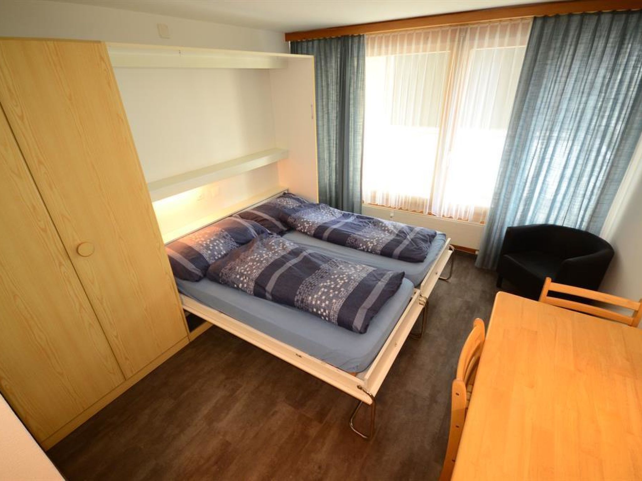 A compact room with a bunk bed, a wooden table, and a chair.
