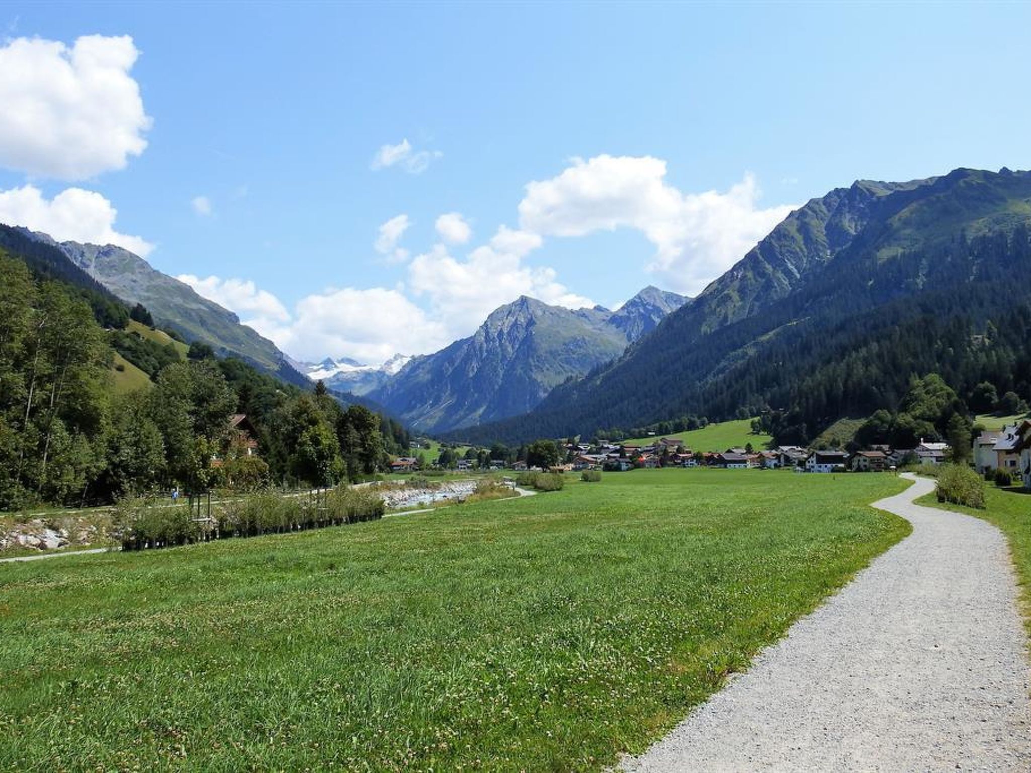 Un paysage rural avec un chemin de gravier, des champs verdoyants et des montagnes en arrière-plan.