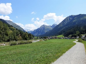 Ländliche Landschaft mit einem Schotterweg, grünen Feldern und Bergen im Hintergrund.