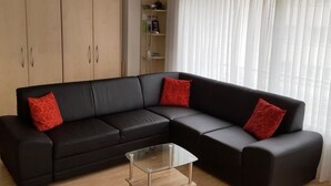 Un canapé d’angle noir avec des coussins rouges, une table basse en verre et un plancher en bois.