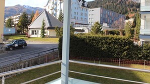 Un immeuble d’habitation doté d’un balcon, une route avec une voiture, et des montagnes en arrière-plan.