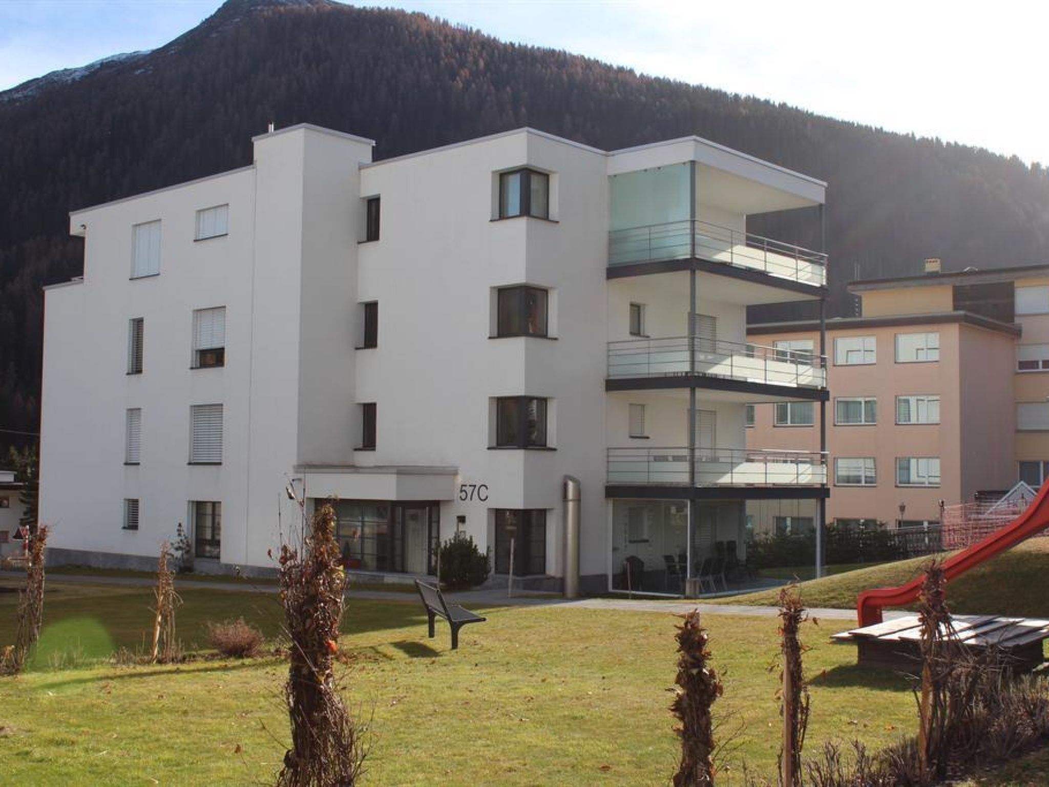 A multi-story building with a flat roof, a balcony on the upper floor, and a sign with the number '57C' indicating a room or unit number.