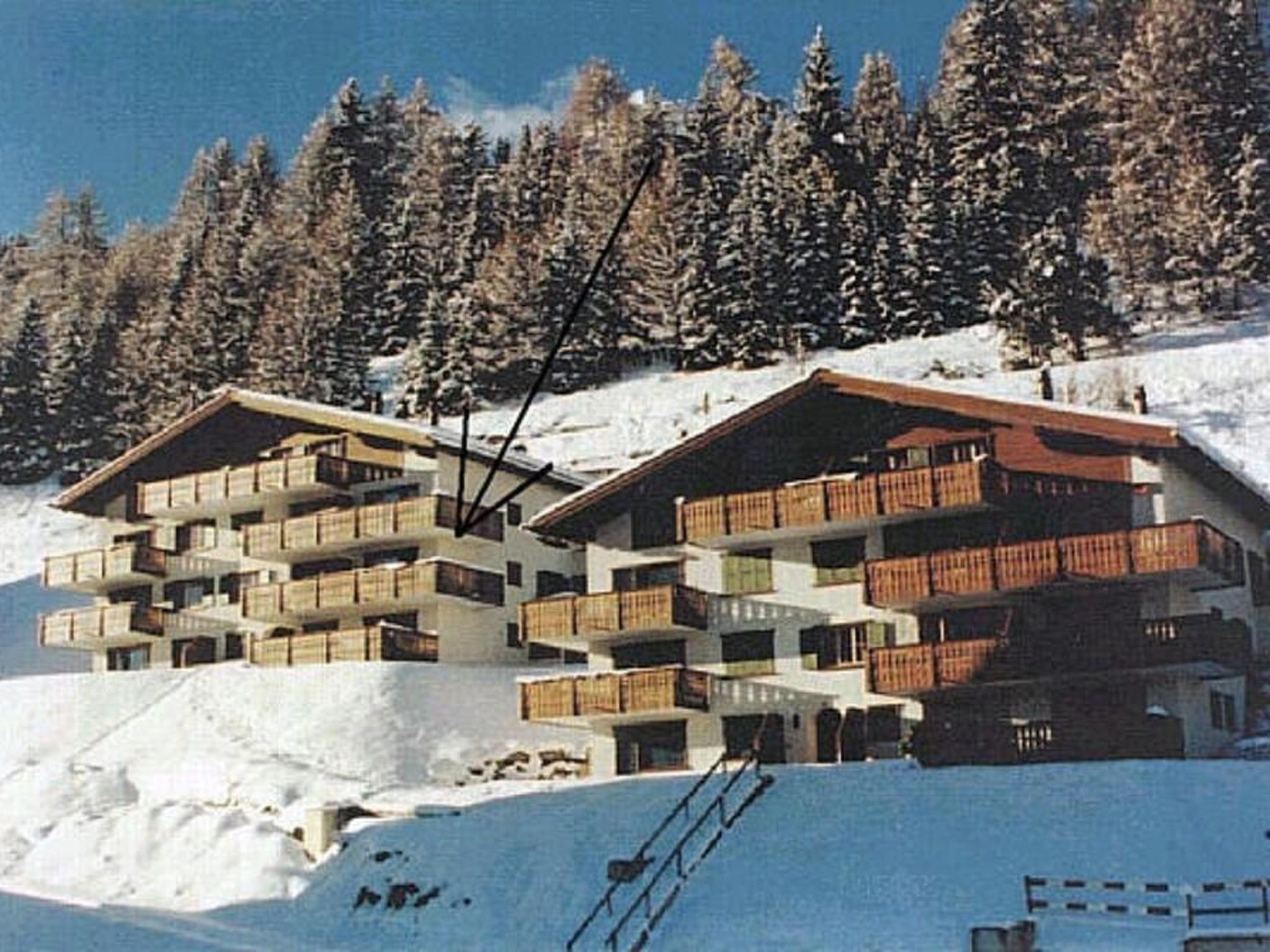 Ein mehrstöckiges Hotel mit Balkonen, eingebettet in einen verschneiten Hang mit Bäumen im Hintergrund.