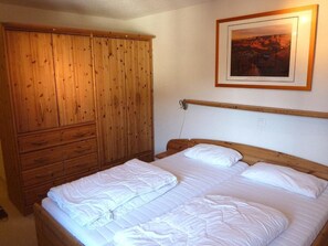 Ein Schlafzimmer mit einem Holzschrank, einem Bett mit weißer Bettwäsche und einem gerahmten Bild an der Wand.