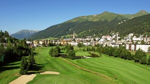 Un campo de golf con un mástil de bandera, rodeado por una zona residencial con casas y una iglesia.
