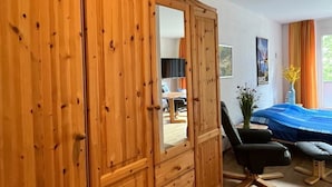 Una habitación con un armario de madera, una cama con cubrecama azul, una silla y un escritorio con un ordenador.