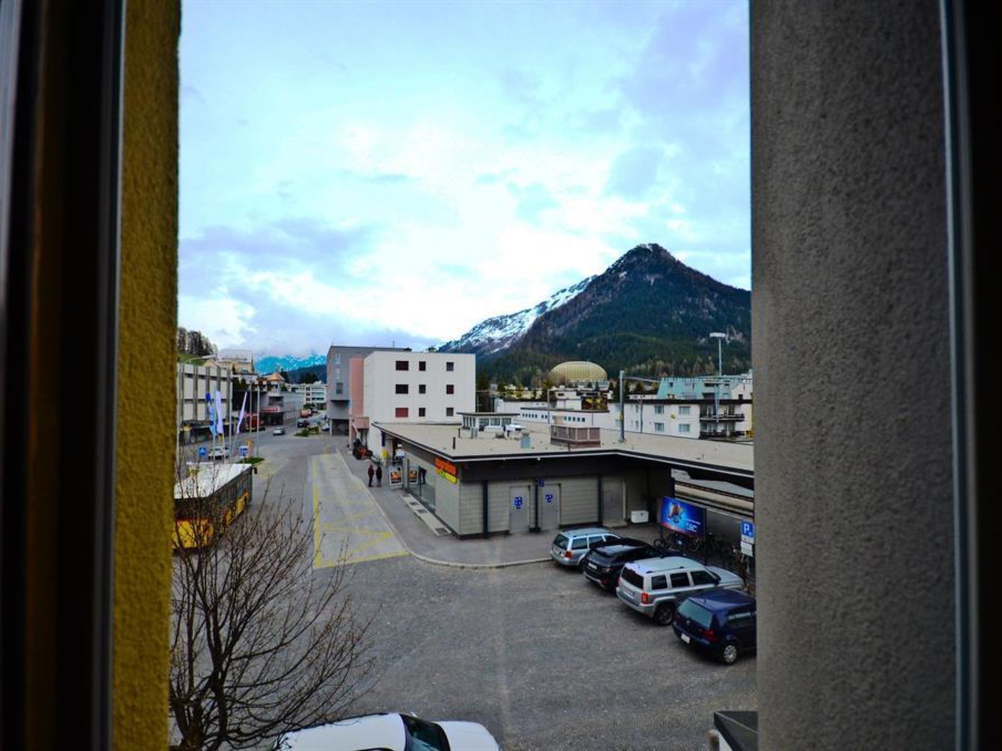 A parking lot with several cars, a building with a flat roof, and a mountain in the background.