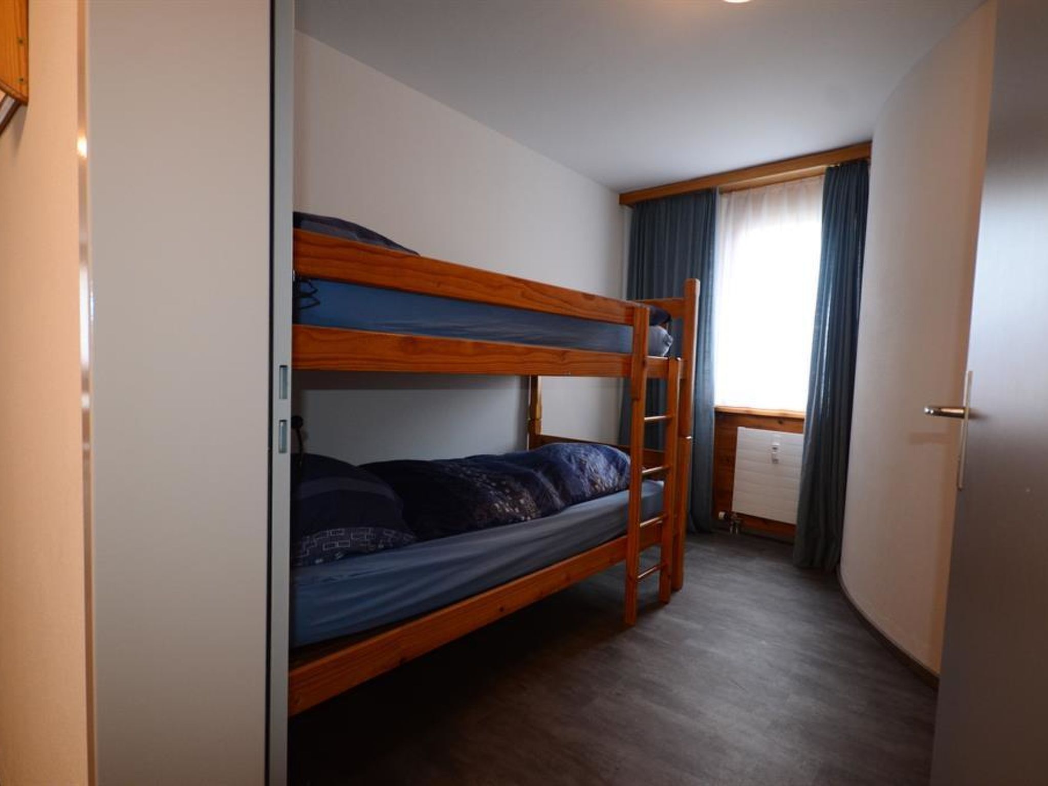 Quarto com beliche, escrivaninha e janela com cortinas.