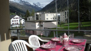 Ein Balkon mit Esstisch, Stühlen und Blick auf Gebäude und Berge.