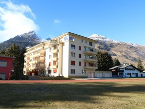A multi-story building with balconies, a red building to the left, and a mountain in the background. - Bündalodge 1015 Appartement/Fewo, Dusche oder Bad, WC 4-Zimmerwohnung by Interhome (Davos)