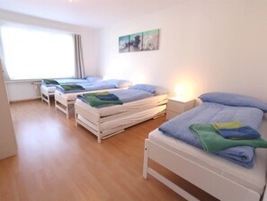 Et hotelværelse med tre senge, et vindue og et kunstværk på væggen.