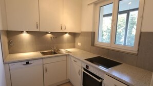 Une cuisine avec des meubles blancs, un évier, une cuisinière et une fenêtre.