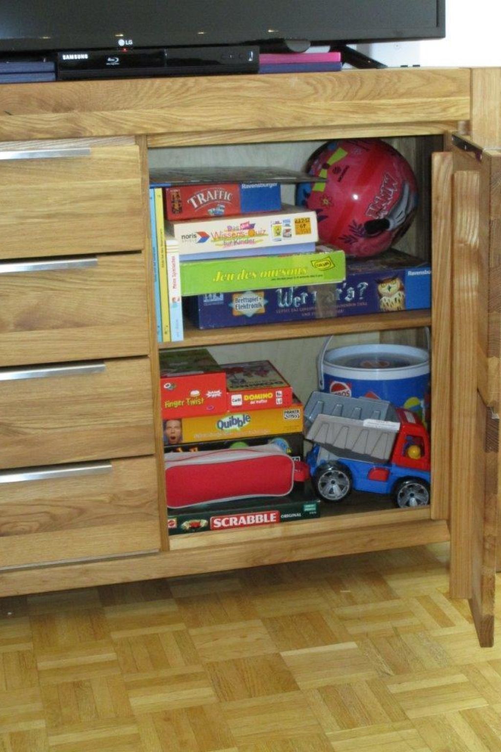 Um armário de madeira com gavetas contendo vários jogos de tabuleiro e um caminhão de brinquedo.