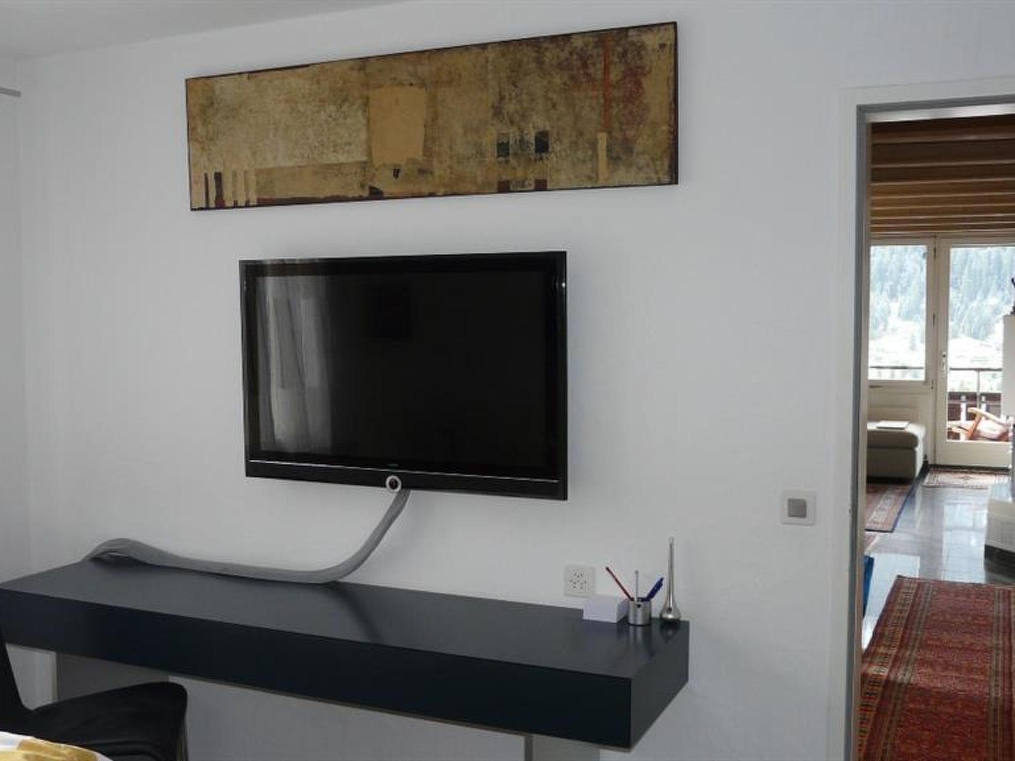 A modern living room with a flat-screen TV mounted on the wall, a black console table, and a large abstract painting above the TV.