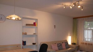 A living room with a sofa, a table, a chair, a bookshelf, a clock, and a ceiling light fixture. - Talstrasse 22 App 26 Appartement/Fewo, Dusche oder Bad, WC 2½-Zimmerwohnung by Interhome (Davos)