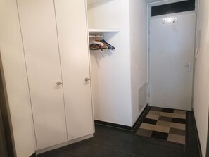 Ein Flur mit einem weißen Kleiderschrank, einer Tür mit Lichtschalter und einer karierten Matte auf dem Boden.