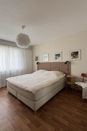 Ein Schlafzimmer mit einem großen Bett, einem Nachttisch, einem Sessel, einer Pendelleuchte und gerahmten Bildern an der Wand.