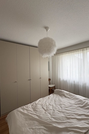 Een slaapkamer met een bed, een kledingkast, een stoel en een plafondlamp.