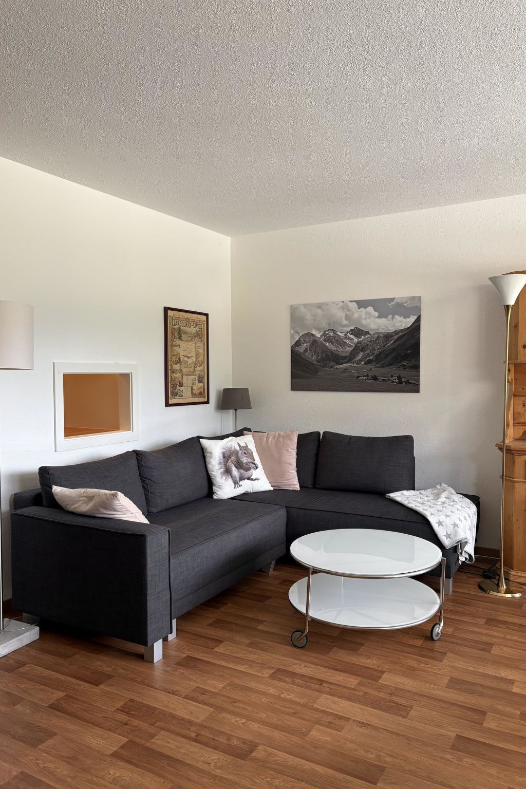 A modern living room with a sectional sofa, a round coffee table, and a mountain landscape painting on the wall.
