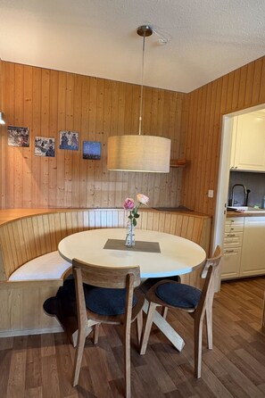 Ein Zimmer mit Holzwandverkleidung, einem runden Tisch, zwei Stühlen, einer Pendelleuchte und einer Bank.