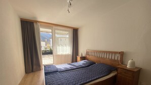 A bedroom with a wooden bed, a nightstand, a lamp, and a view of the outdoors. - Talstrasse 22 App 13 Appartement/Fewo, Dusche oder Bad, WC 3½-Zimmerwohnung by Interhome (Davos)