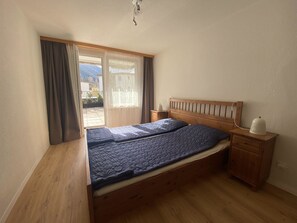 A bedroom with a wooden bed, a nightstand, a lamp, and a view of the outdoors. - Talstrasse 22 App 13 Appartement/Fewo, Dusche oder Bad, WC 3½-Zimmerwohnung by Interhome (Davos)