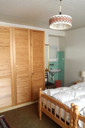 A bedroom with a wooden bed frame, a wooden wardrobe, a bathroom with a sink, and a hanging light fixture. - Chesa Nova 13 Appartement/Fewo, Dusche oder Bad, WC 2 1/2-Zimmerwohnung by Interhome (Davos)