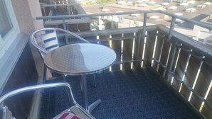 Ein Balkon mit rundem Tisch und zwei Stühlen, eine Holzlattenveranda und Blick auf den Parkplatz.
