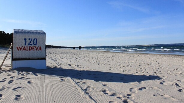 A beach with a sign reading '120 WALDEVA' and footprints in the sand.