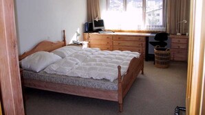Un dormitorio con una cama de madera, un escritorio con una computadora, una silla y una ventana con cortinas.