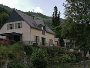 Ein zweistöckiges Haus mit einem Balkon, einer Steinmauer und Blick auf einen Hügel.