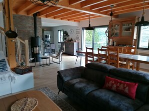 Ein geräumiger Wohnbereich mit einem schwarzen Ledersofa, einem Holzesstisch und einer Küche im Hintergrund.
