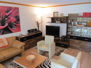 Ein Wohnzimmer mit einer Couch, einem Couchtisch, einem Fernseher und einem Bücherregal.
