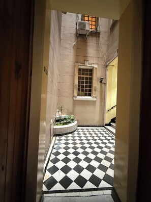 A narrow corridor with a checkered floor, a window with shutters, and a small planter with plants. - Cozy 1-bedroom apartment in beautiful Buenos Aires with AC (Buenos Aires)