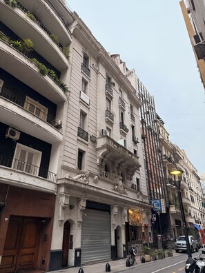Ein mehrstöckiges Gebäude mit Balkonen, einer geschlossenen Garagentür und einer Straße mit parkenden Autos und einem Motorrad.