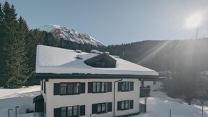 Un edificio a due piani con un tetto imbiancato dalla neve, immerso in un paesaggio innevato con una montagna sullo sfondo.