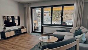 Un soggiorno moderno con una TV a schermo piatto, un divano, un tavolino da caffè e vista sull'esterno.