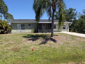 A single-story house with a front porch, a small front yard, and a palm tree.