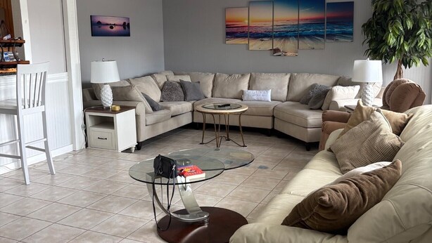 Ein Wohnzimmer mit einem Ecksofa, einem Glastisch, einem Deckenventilator und Wandbildern.