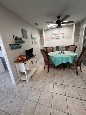 A dining area with a table set for four, a ceiling fan, and artwork on the walls.